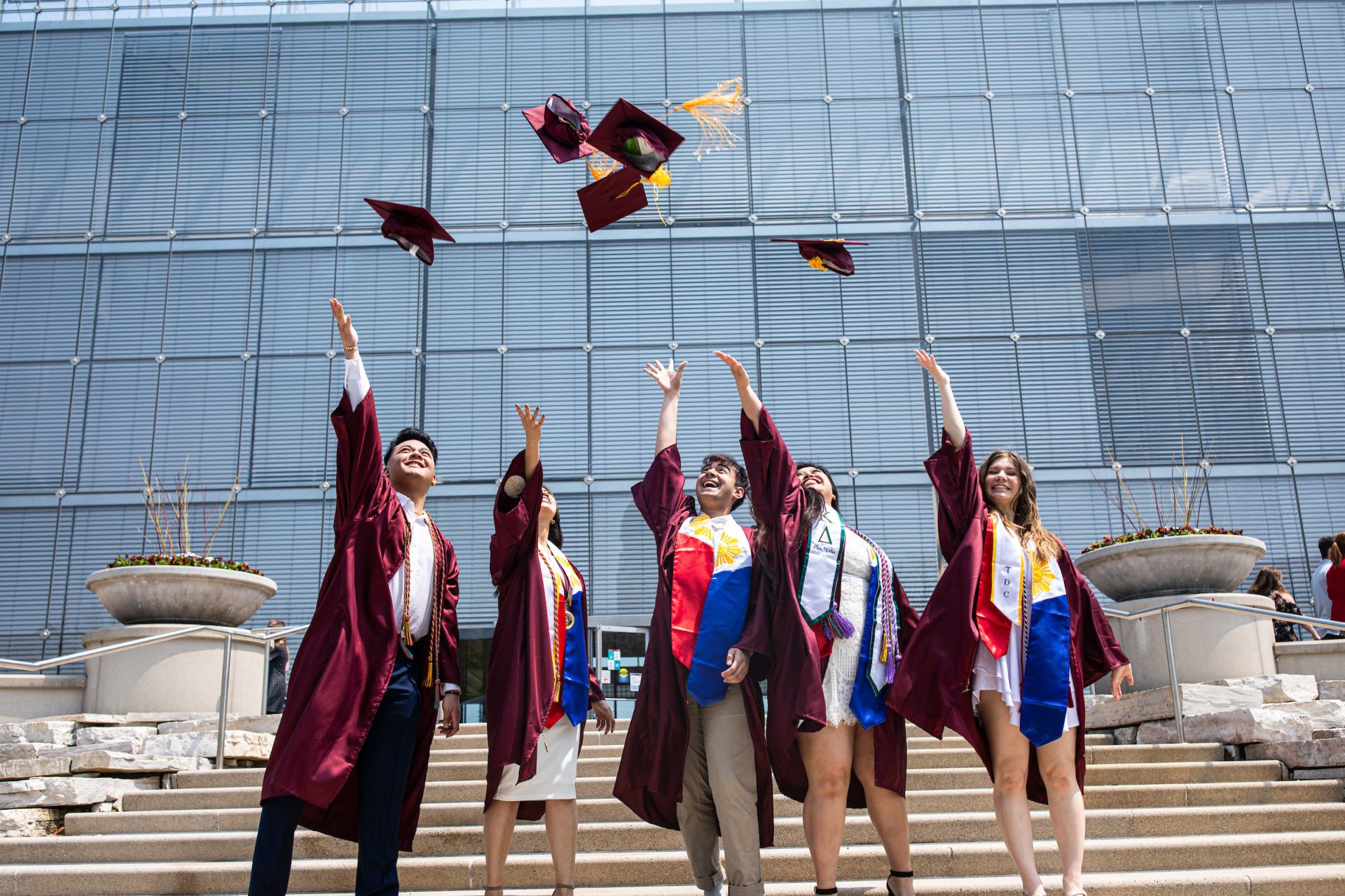 A group of Loyola University Chicago graduates wearing graduation regalia smile and toss their graduation caps into the air