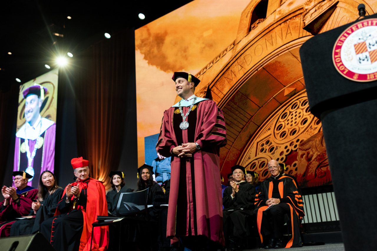 President Mark C. Reed on stage in academic regalia, smiling