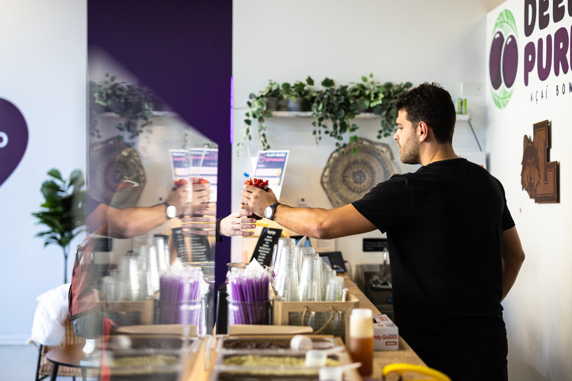 A man wearing a black shirt hands a smoothie across the counter to a customer