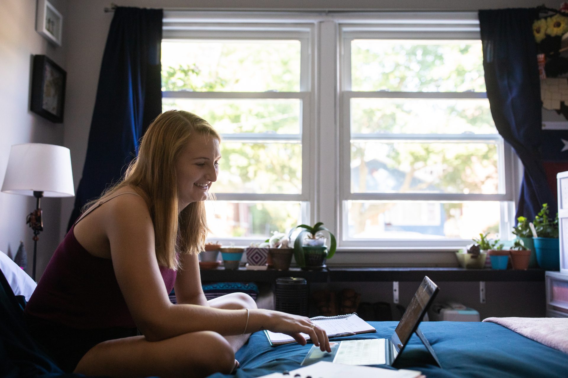 Girl sitting on bed working on a laptop.
