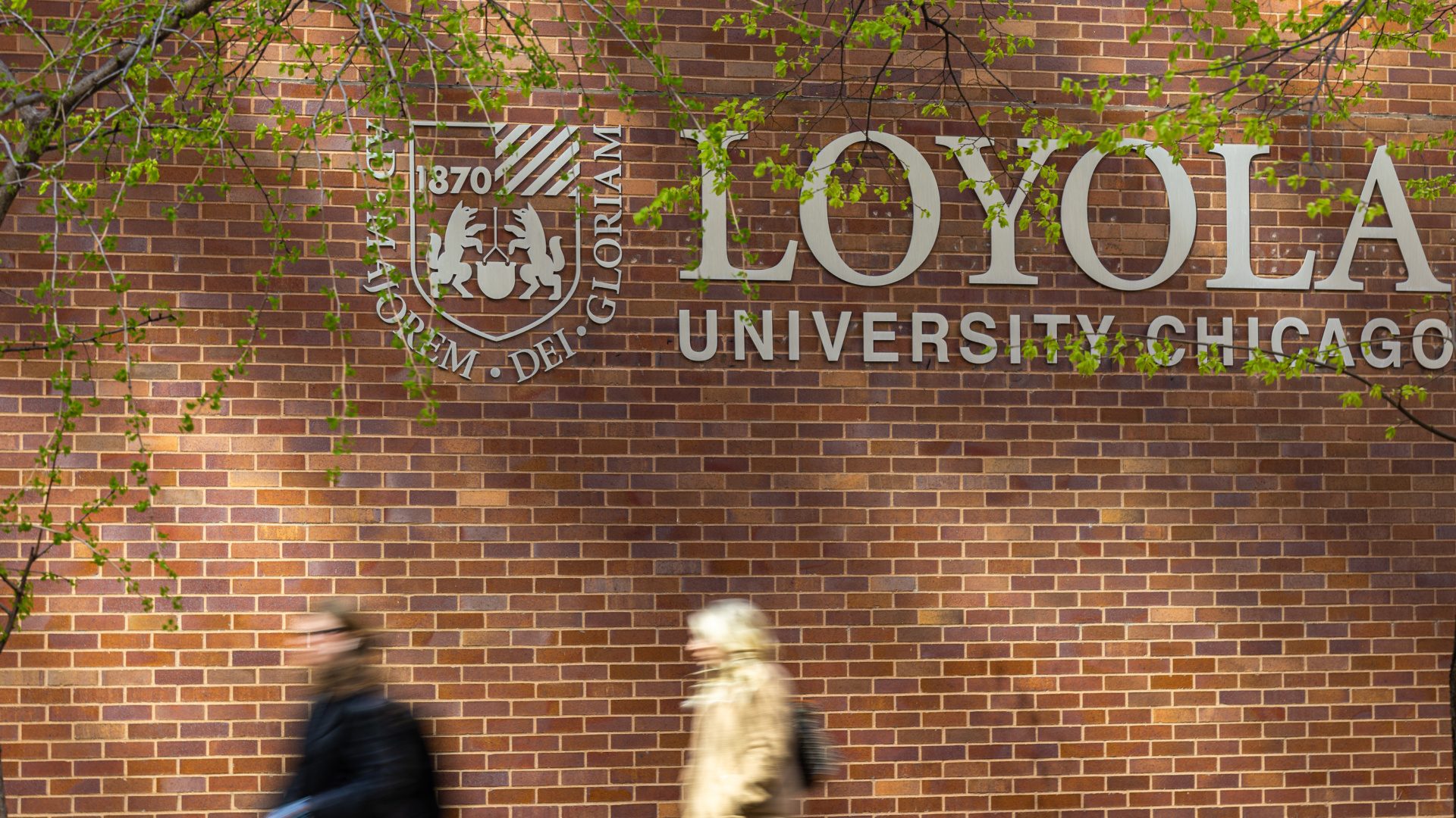 Two people walk by a campus sign for Loyola University Chicago