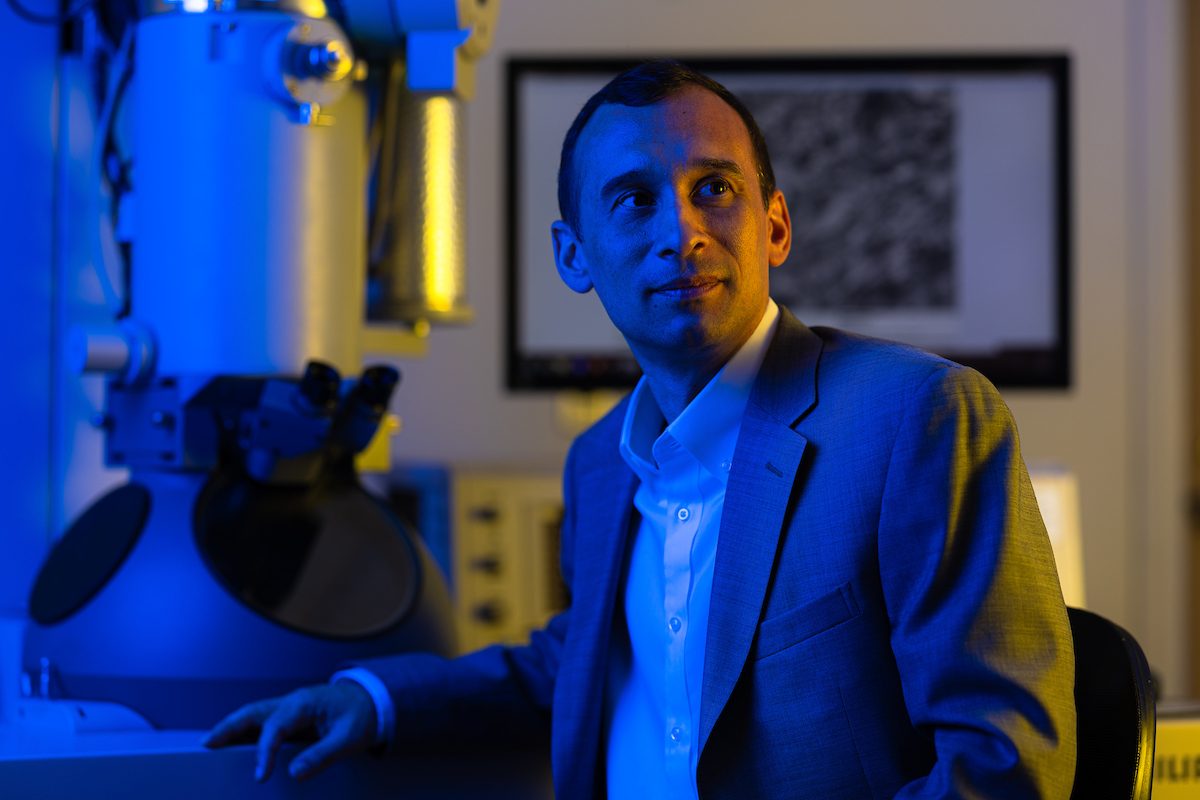 A man sits in blue and yellow lighting next to a large microscope