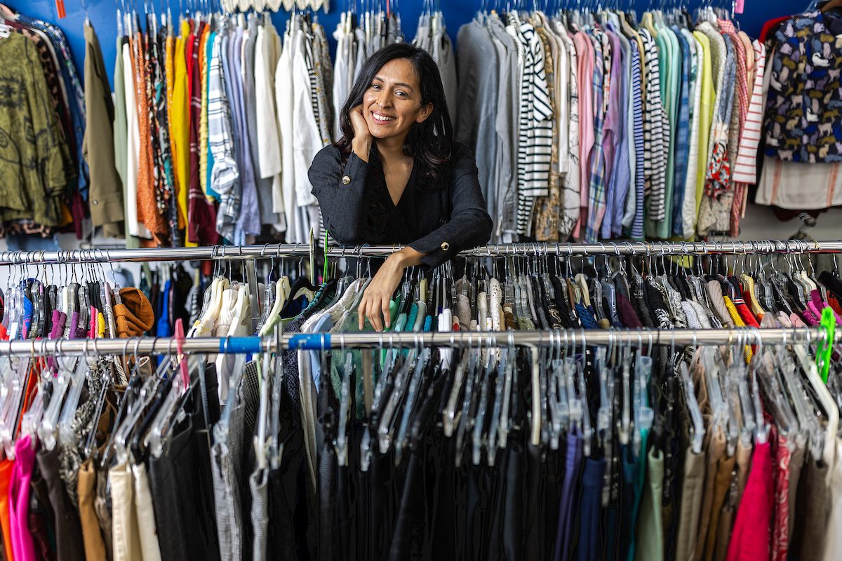 A woman poses between racks of clothing and rests her chin on her hand