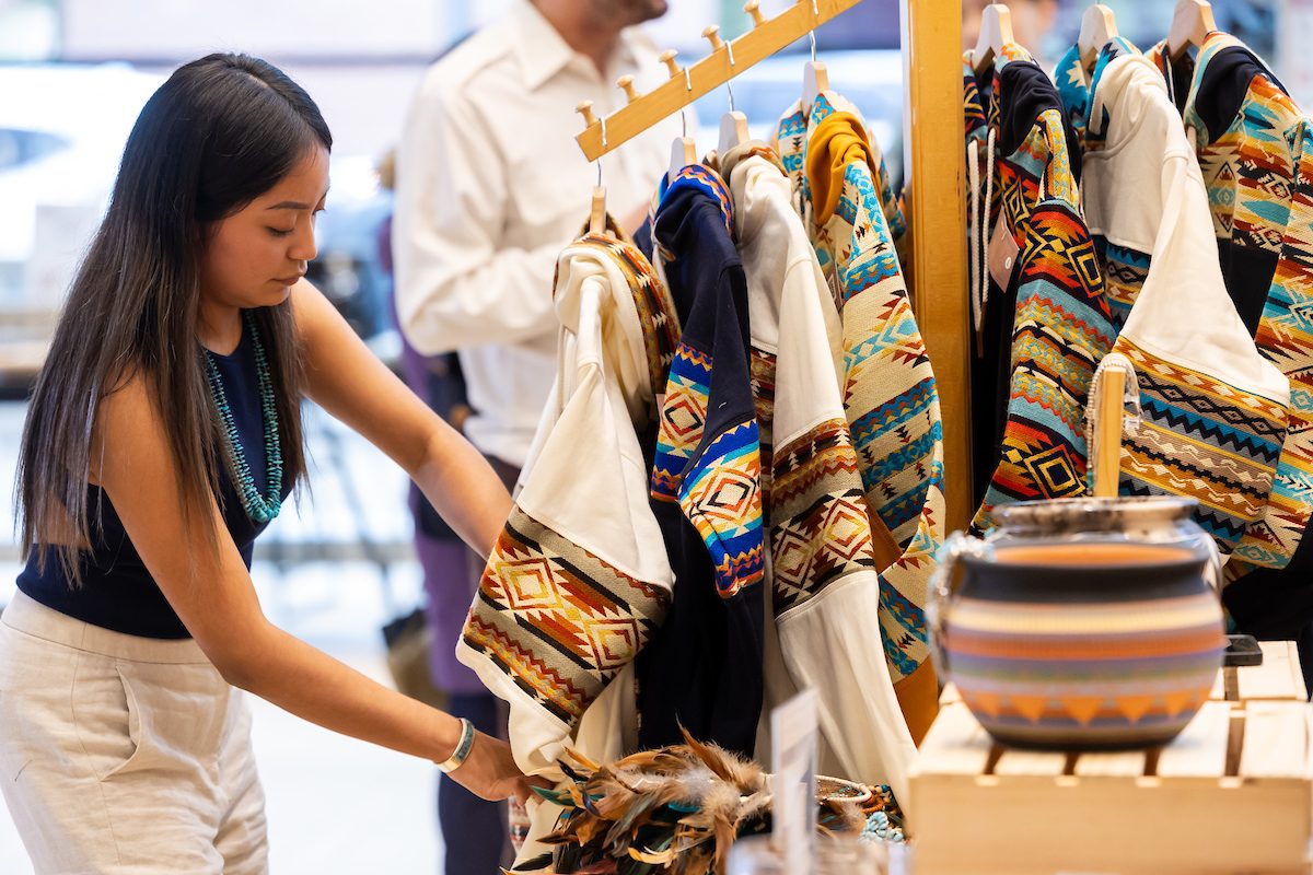 Quinlan School of Business students participate in the Side Hustle Showcase, designed to shine a spotlight on the innovative and enterprising endeavors of Loyola University Chicago students. Selected students showcase their entrepreneurial *side hustles* for judges to pick a winner. (Photo: Lukas Keapproth) A Loyola University Chicago student sets up patterned jackets on hangers at a tabling event