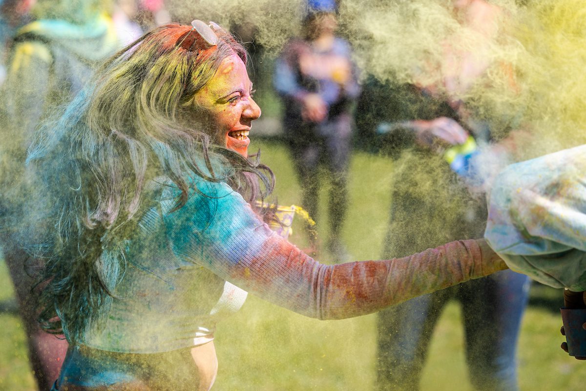 The Hindu Student Association hosts the annual Holi celebration in the Winthrop Play Lot, celebrating the arrival of spring, on April 6, 2024. (Photo by: Lukas Keapproth) A Loyola University Chicago student covered in multicolored powders smiles as she throws powder at another student