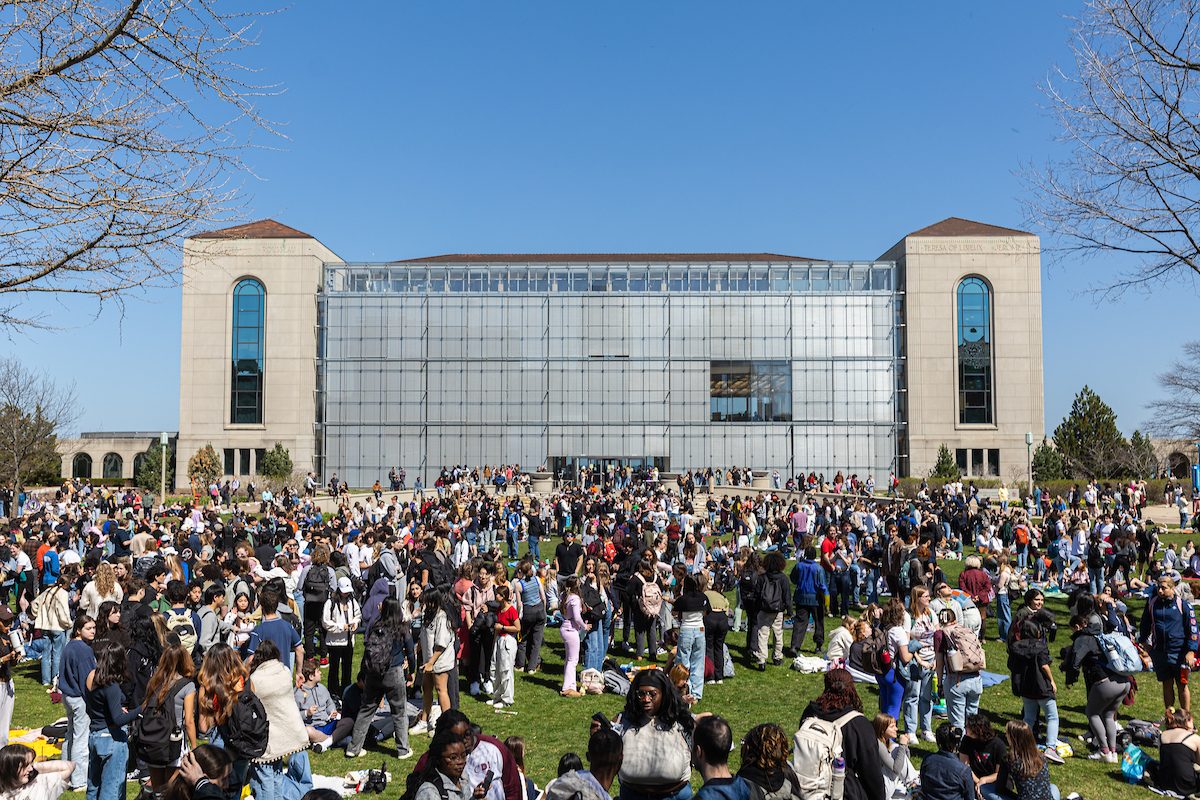 The Loyola University Chicago community gathered at the Lake Shore Campus to witness the historic, near total solar eclipse on April 8, 2024. (Photo: Lukas Keapproth) A large crowd of Loyola University Chicago studnts stand outside on a sunny day in front of a large glass-walled building