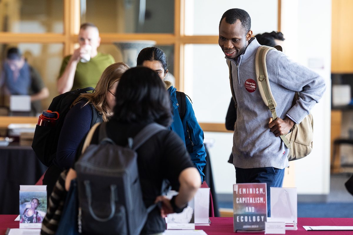 University Libraries hosts the annual Faculty Scholarship Celebration event in Information Commons on April 18, 2024. (Photo by: Lukas Keapproth) Loyola University Chicago students wearing backpacks stand around a rectangular table displaying books and speak to each other