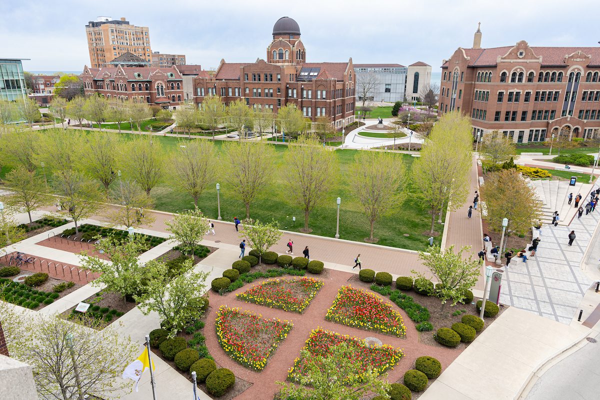 Spring colors come alive on the Lake Shore Campus during finals week, April 23, 2024 .(Photo: Lukas Keapproth) Red-brick buildings stand around a green quad lined with trees on Loyola University Chicago's campus