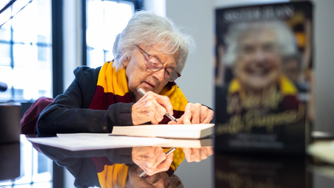 An older woman wearing a Loyola University Chicago scarf signs a book