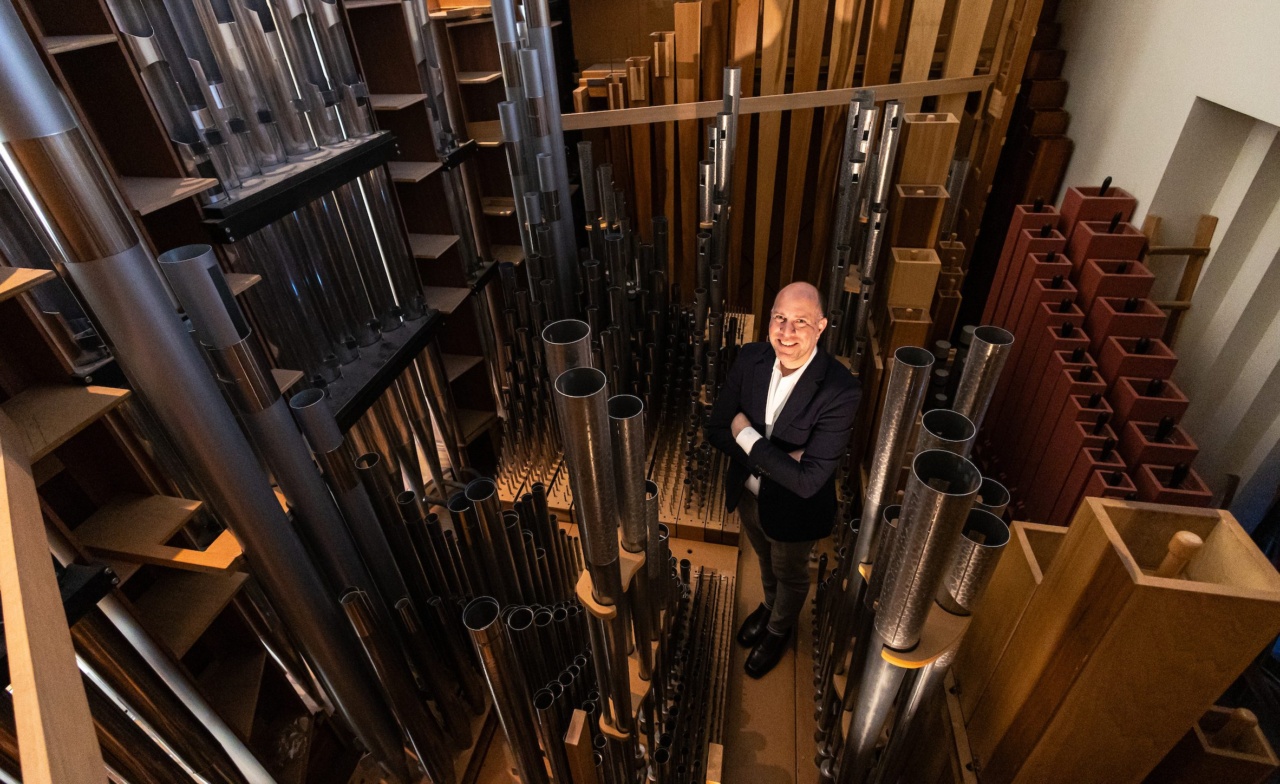 A man wearing a black suit and white shirt crosses his arms and grins from the inside of a large pipe organ in the Loyola University Chicago chapel