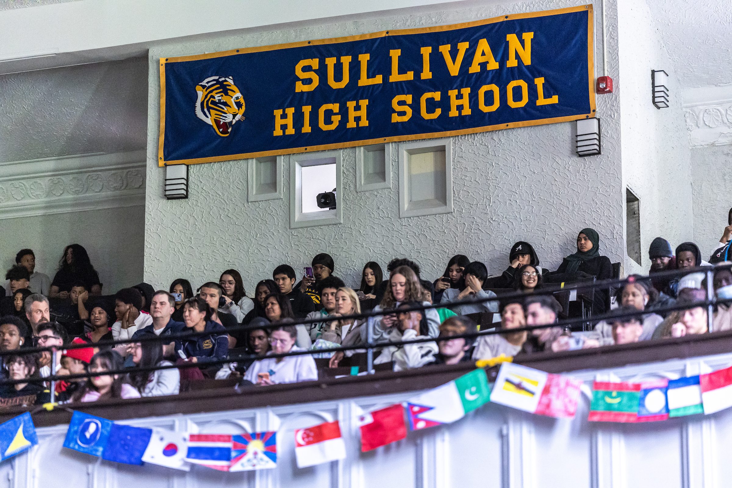 An audience watches a stage with a banner reading Sullivan High School in the background