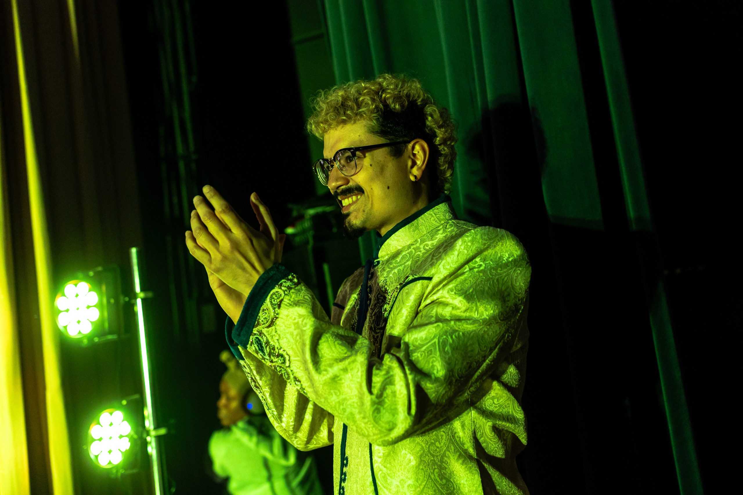 A Loyola University Chicago alum stands backstage during a show and claps for the performers