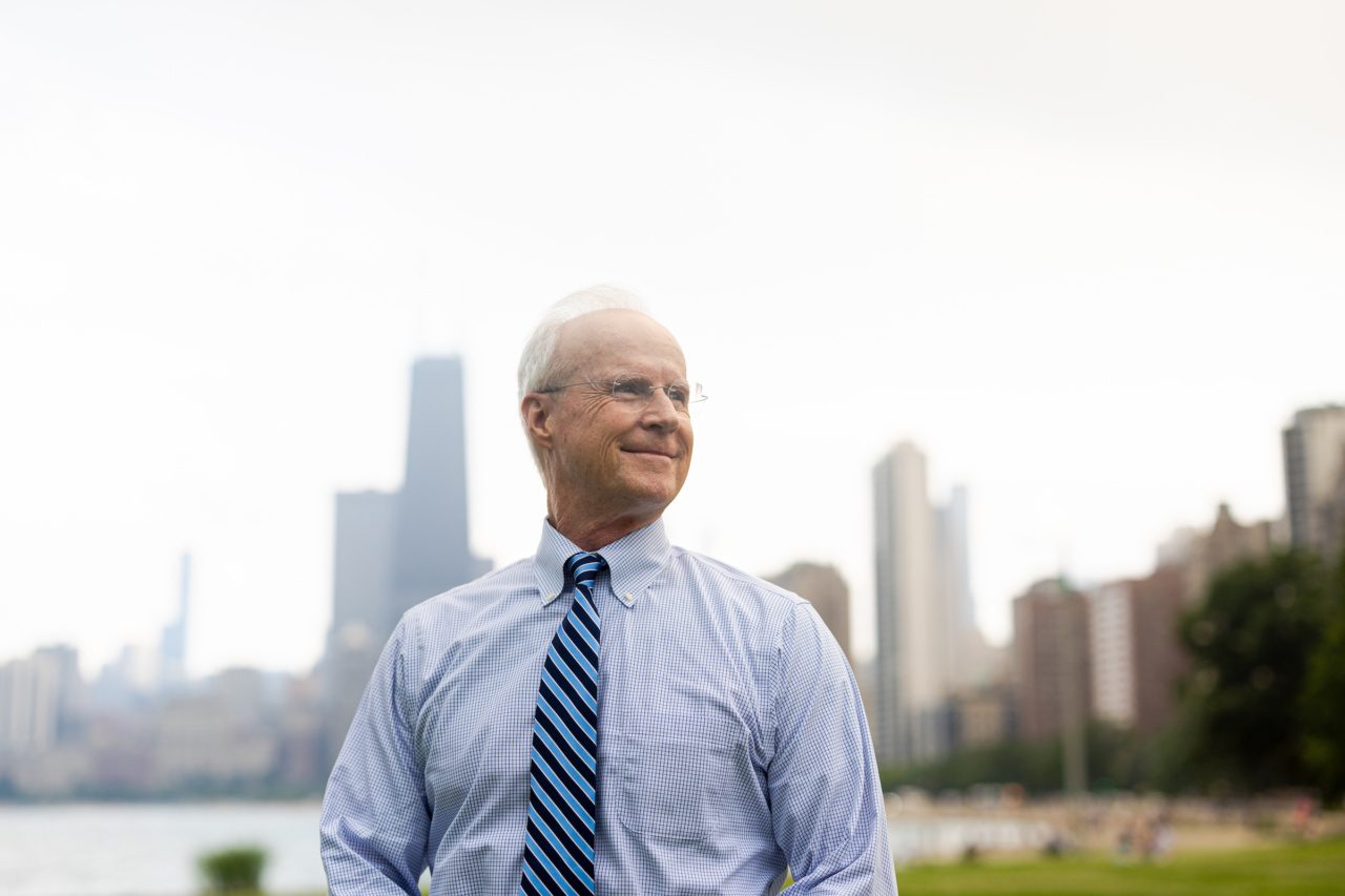 A man wearing a striped tie looks into the distance with the Chicago skyline in the background