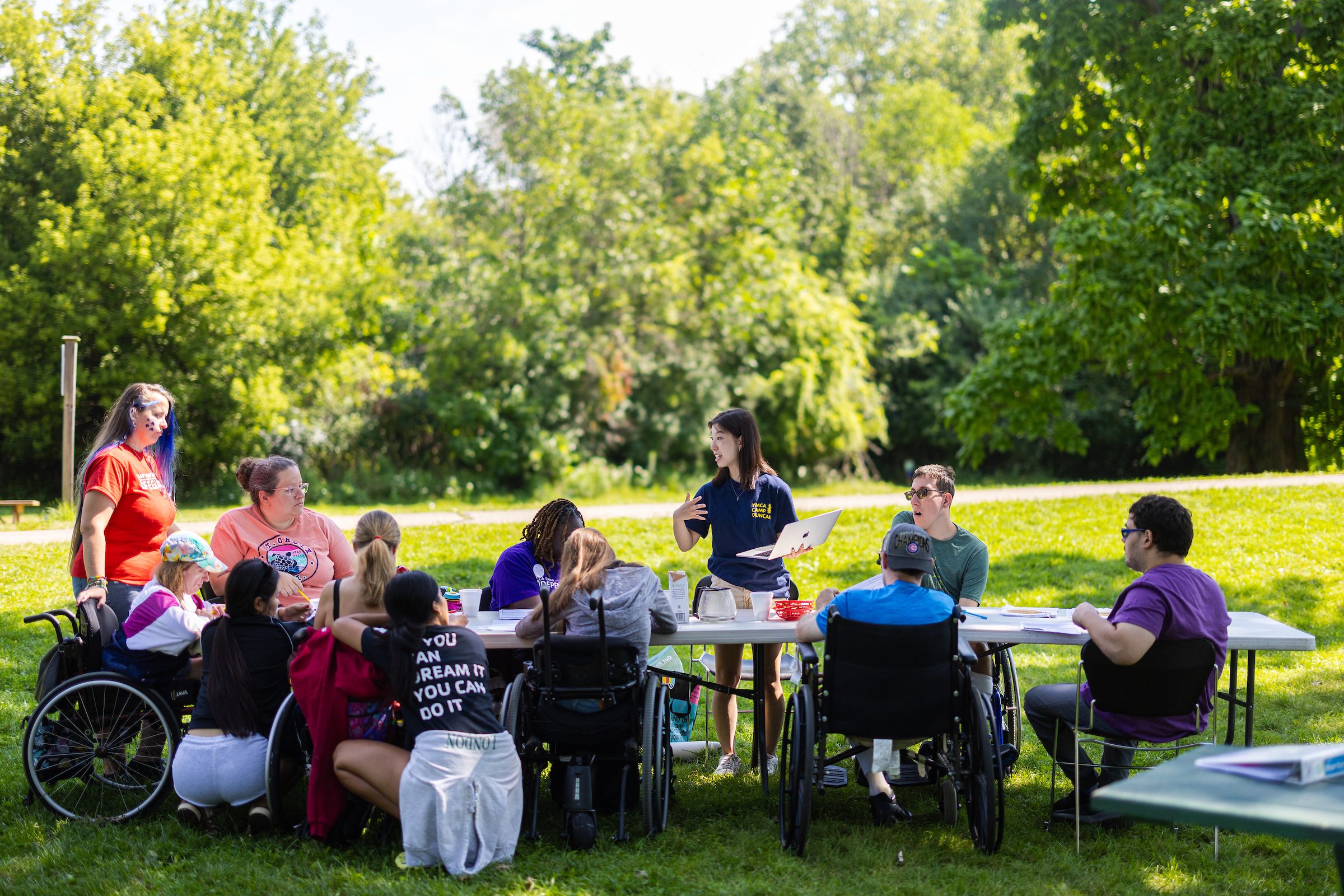 A group of people using wheelchairs sit outdoors at a picnic table