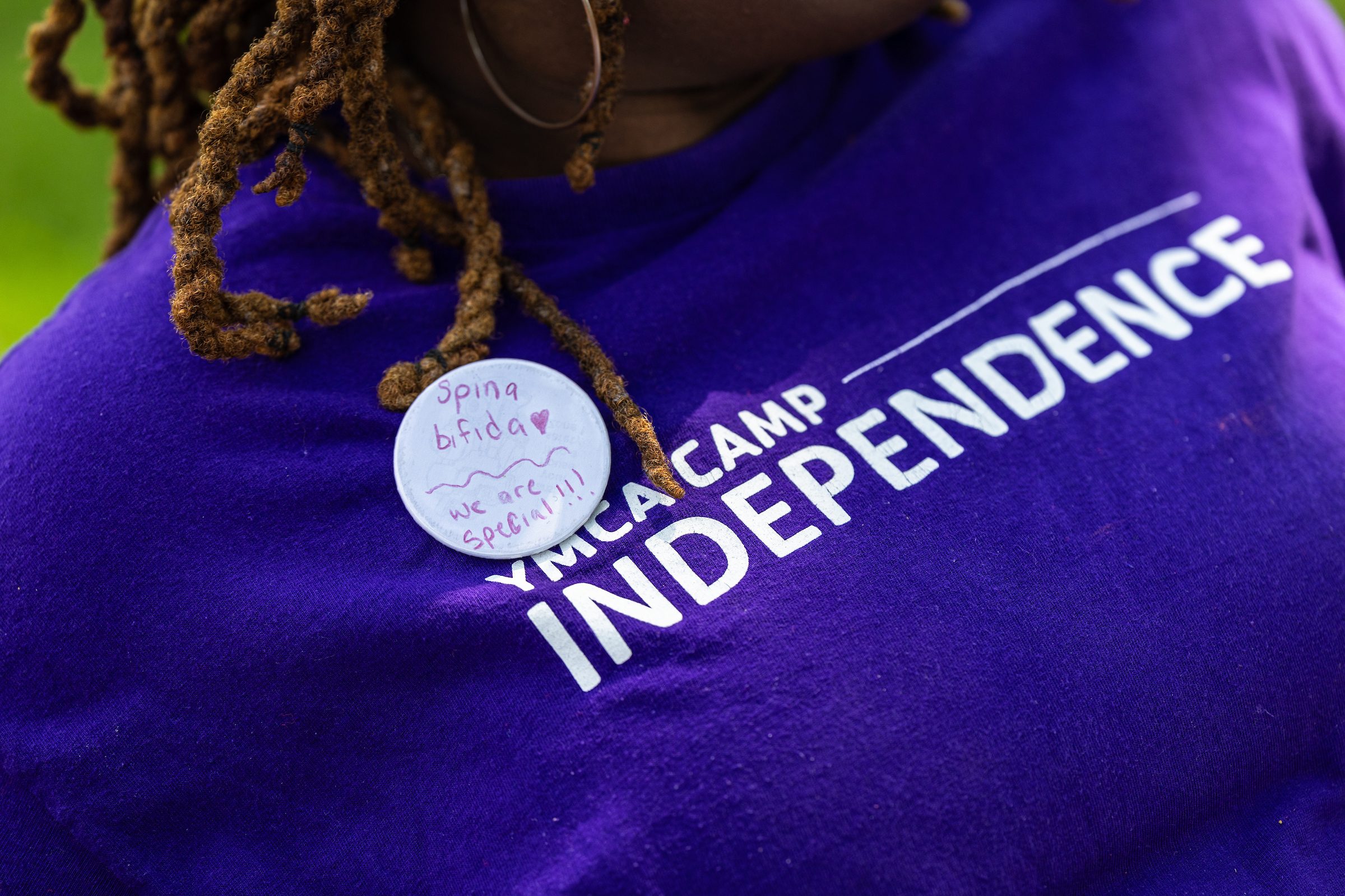 A woman wears a Camp Independence T-shirt with a pin that reads "spina bifida - we are special!!!"