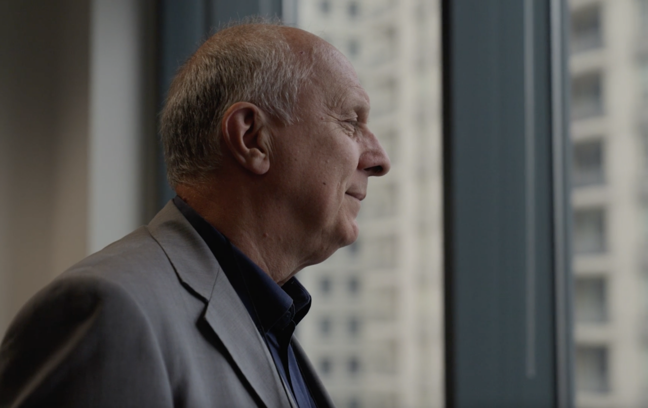 A man wearing a suit takes in a view of skyscrapers outside a high rise window