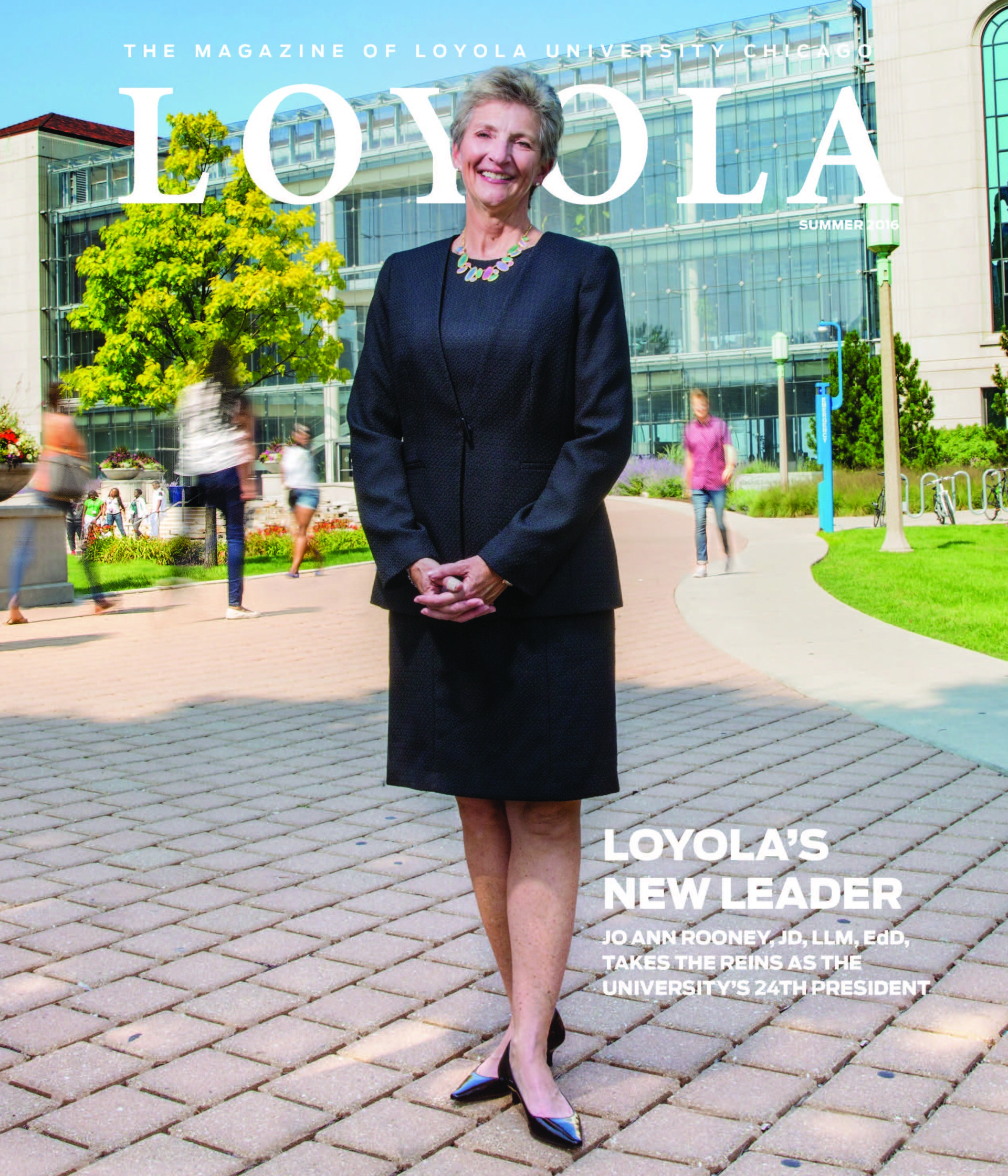 A woman wearing a skirt and a blazer stands in front of the Loyola University Chicago campus library and smiles on this cover of Loyola magazine