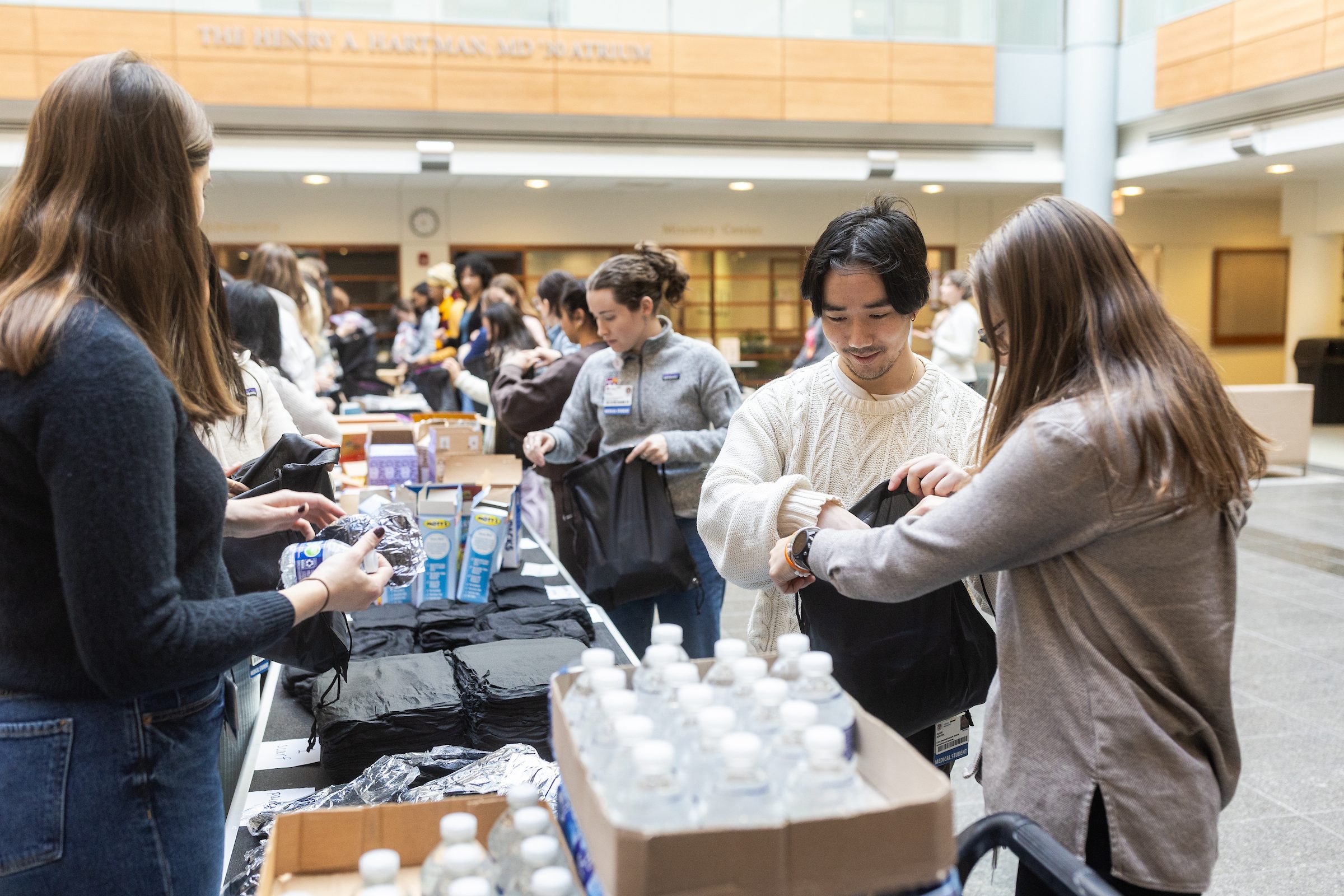 Stritch School of Medicine students and faculty volunteer to assemble hygiene kits for Loyola's Street Medicine Program as part of Martin Luther King Service Days on January 21, 2025. Loyola University Chicago students stand along the length of folding tables and pass items down an assembly line