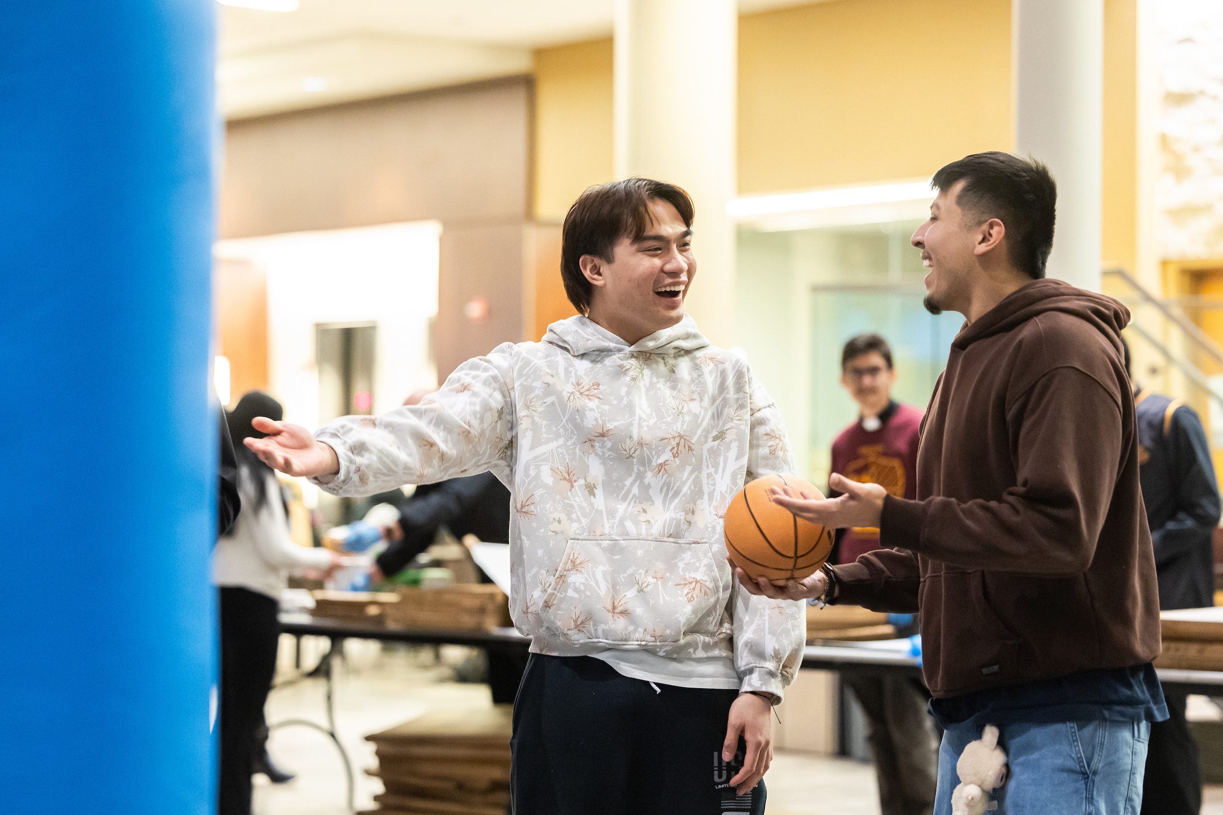 This year’s Jesuit Jam event featured an inflatable bungee run, a Connect 4-style basketball game, and an interactive bingo game. Loyola University Chicago students share a laugh at a campus event in the student center with folding tables in the background.