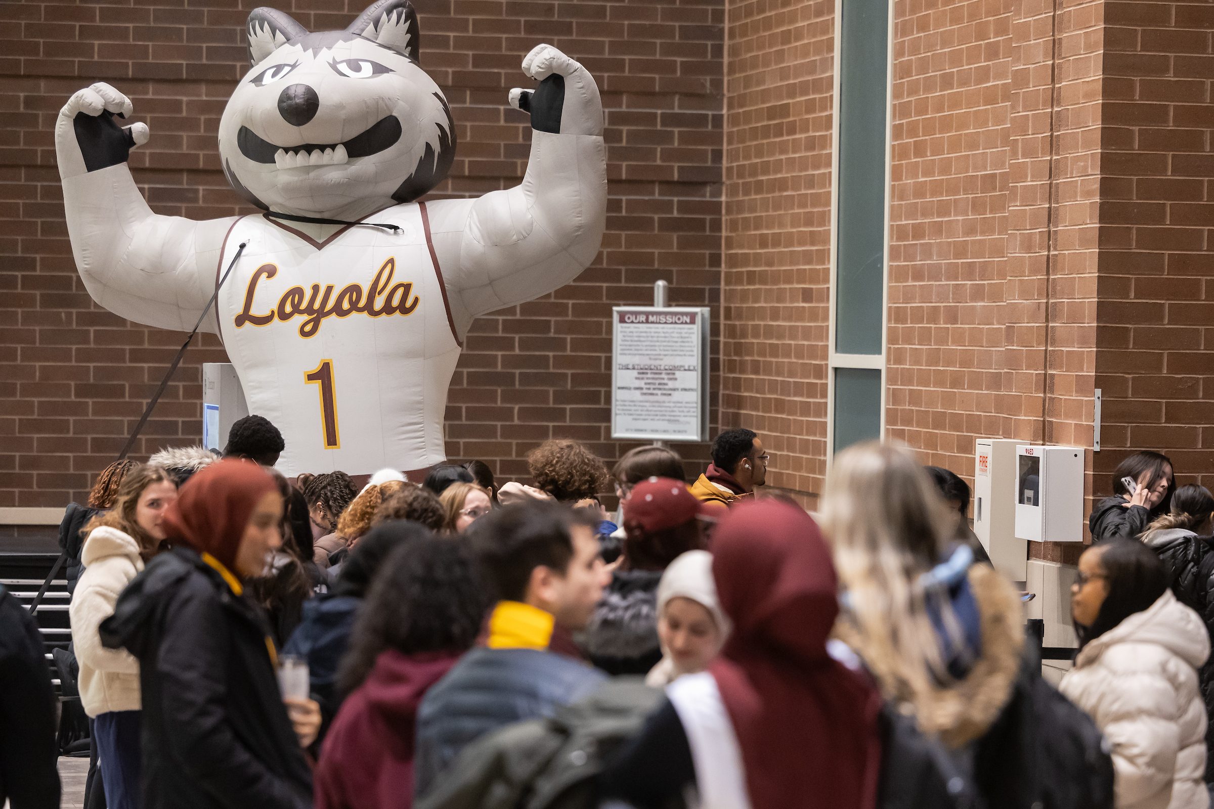 Loyola University Chicago students gather in Damen Hall for the annual Jesuit Jam event. Loyola University Chicago students gather near a large inflatable wolf mascot wearing a Ramblers basketball jersey.