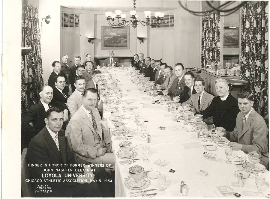 The 1954 Loyola Debate Society poses for a photo at a celebratory dinner after winning a debate event. (Courtesy photo/Loyola University Chicago Archives) A group of Loyola University Chicago students seated at a long table in an ornate room with bowls of ice cream in front of them