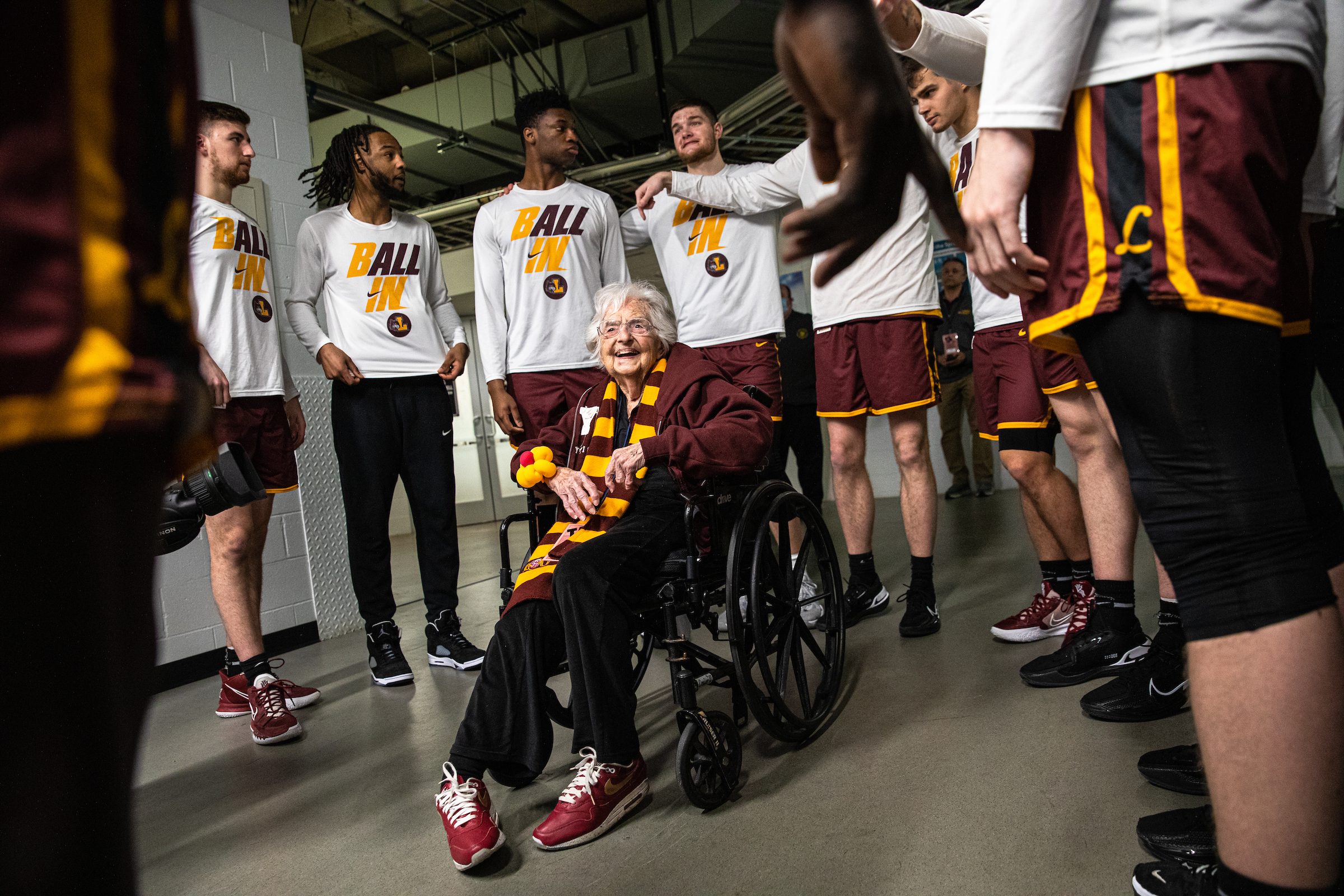 Sister Jean smiles as she sits in a wheelchair with Loyola University Chicago men's basketball players circled around her