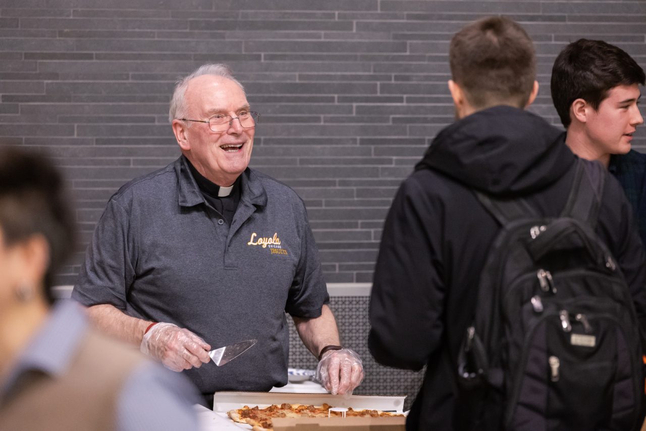 Father T. Jerome Overbeck grins as he serves pizza to a student at a Loyola University Chicago event