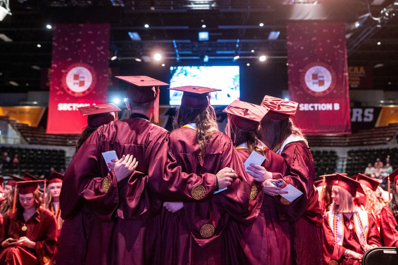 Loyola University Chicago graduates standing with their arms around each other backs