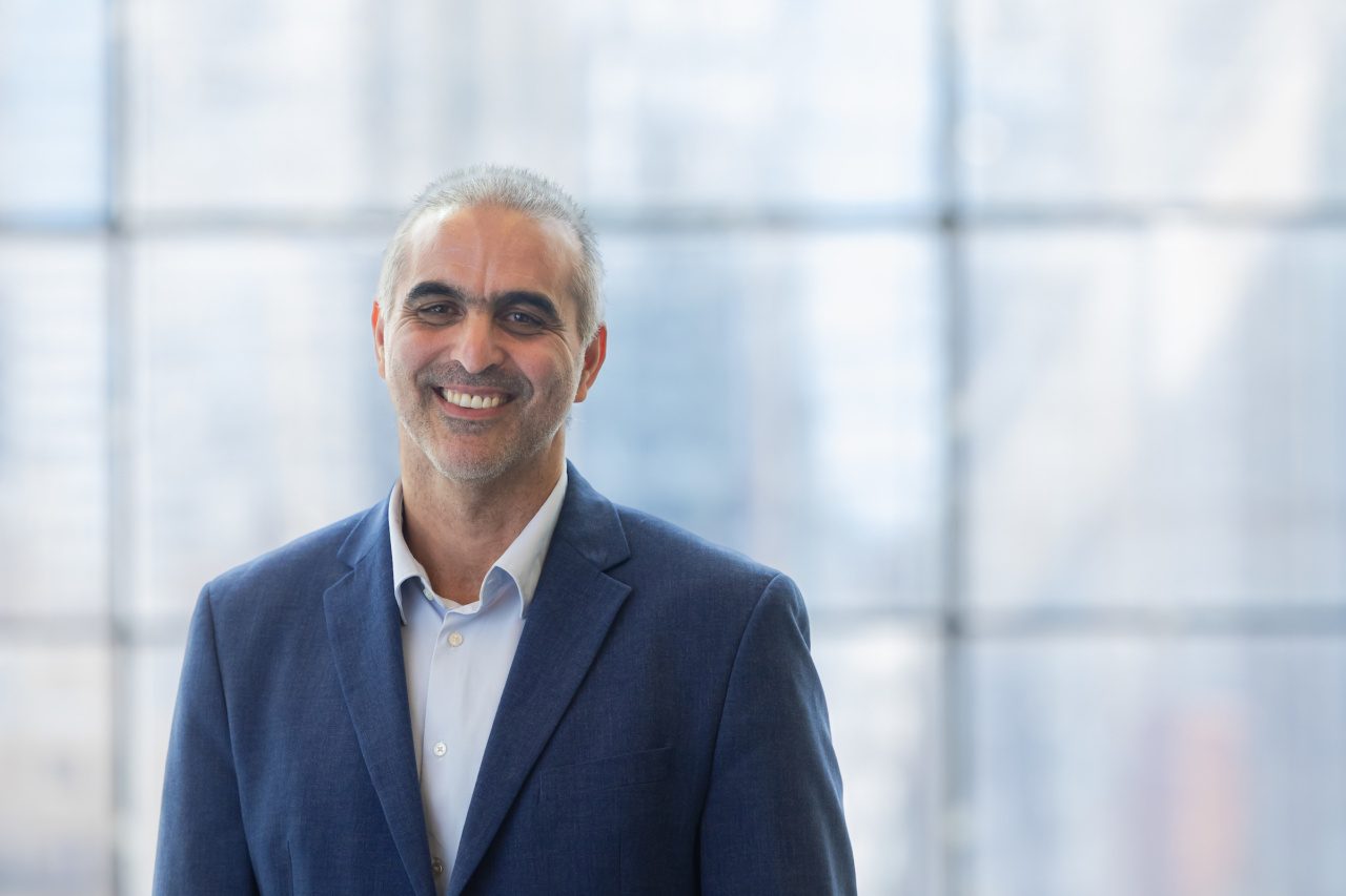 Loyola University Chicago alumnus Pablo Di Si smiles for a portrait with a wall of windows in the background