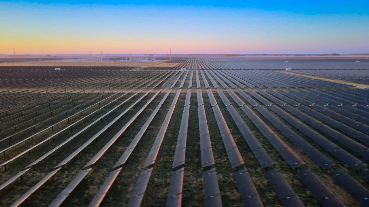 An aerial view image shows fields of solar panels with a colorful sunset in the background.