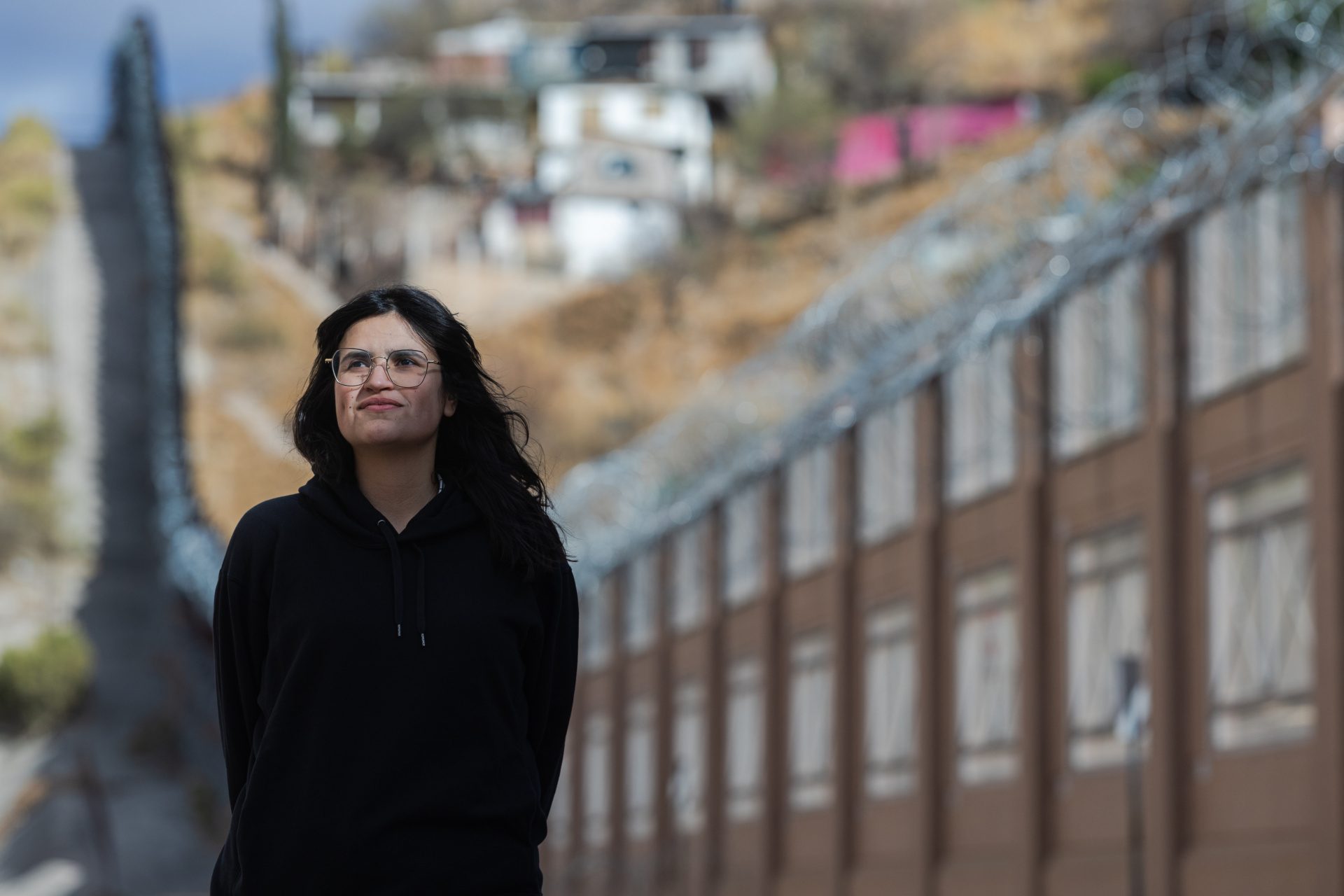 A Loyola University Chicago student stands in front of the wall between the U.S. and Mexico