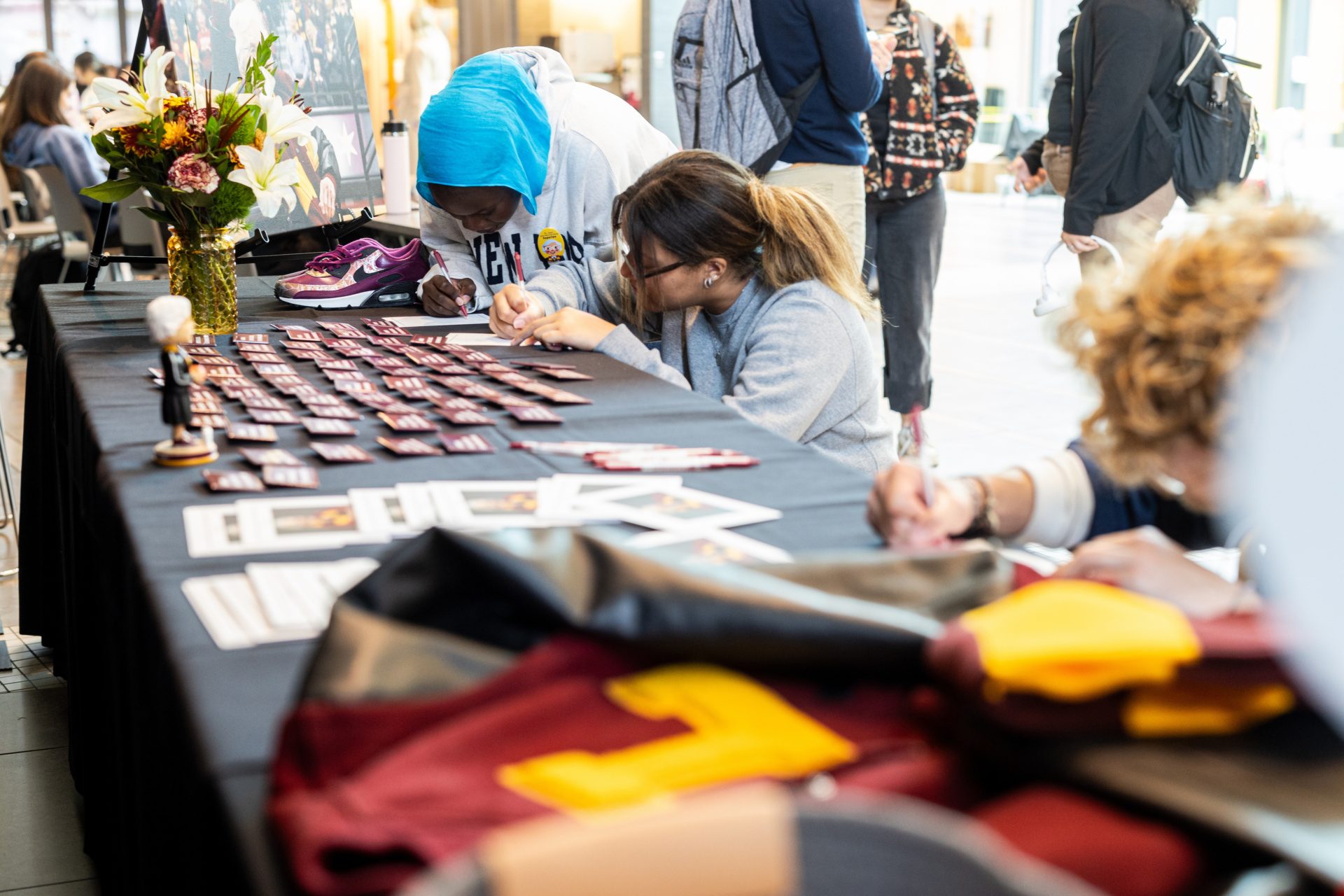 Loyola University Chicago students lean over a table laden with pins, prayer cards, and Loyola memorabilia and write remembrances for Sister Jean
