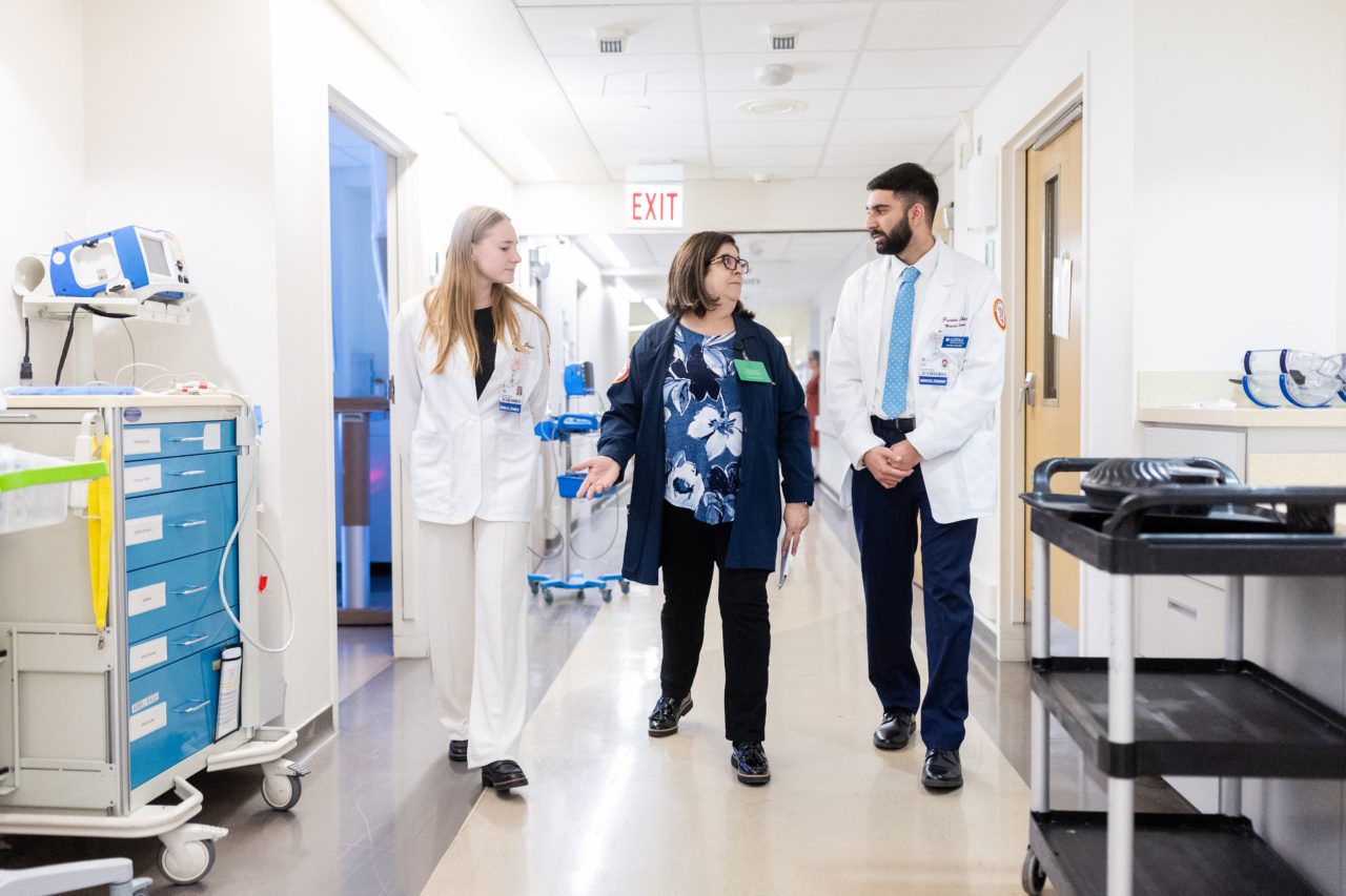 Two Loyola University Chicago students wearing white coats accompany a professor as they walk down a hallway in a hospital