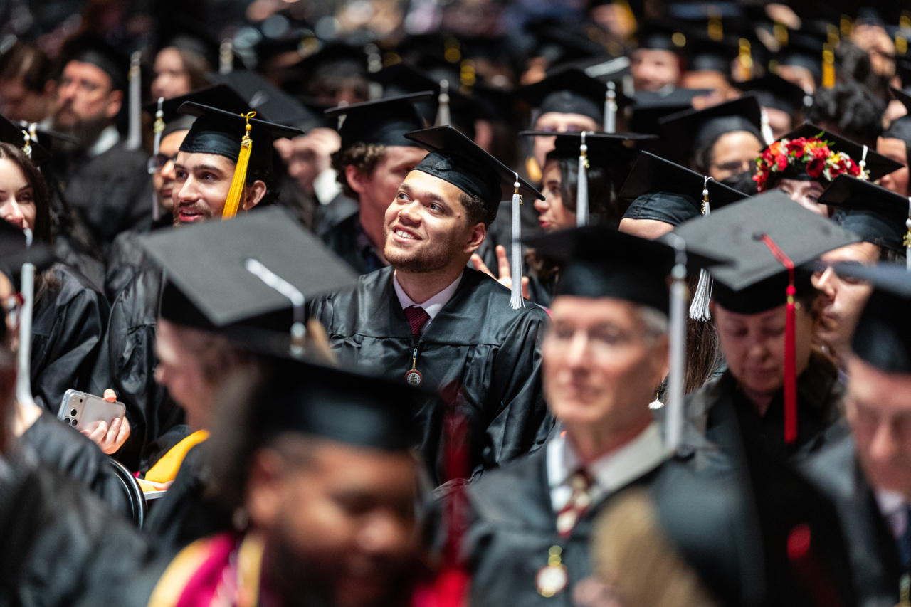 A man wearing a graduation cap and gown looks up and smiles in a crowd of other graduates from Loyola University Chicago