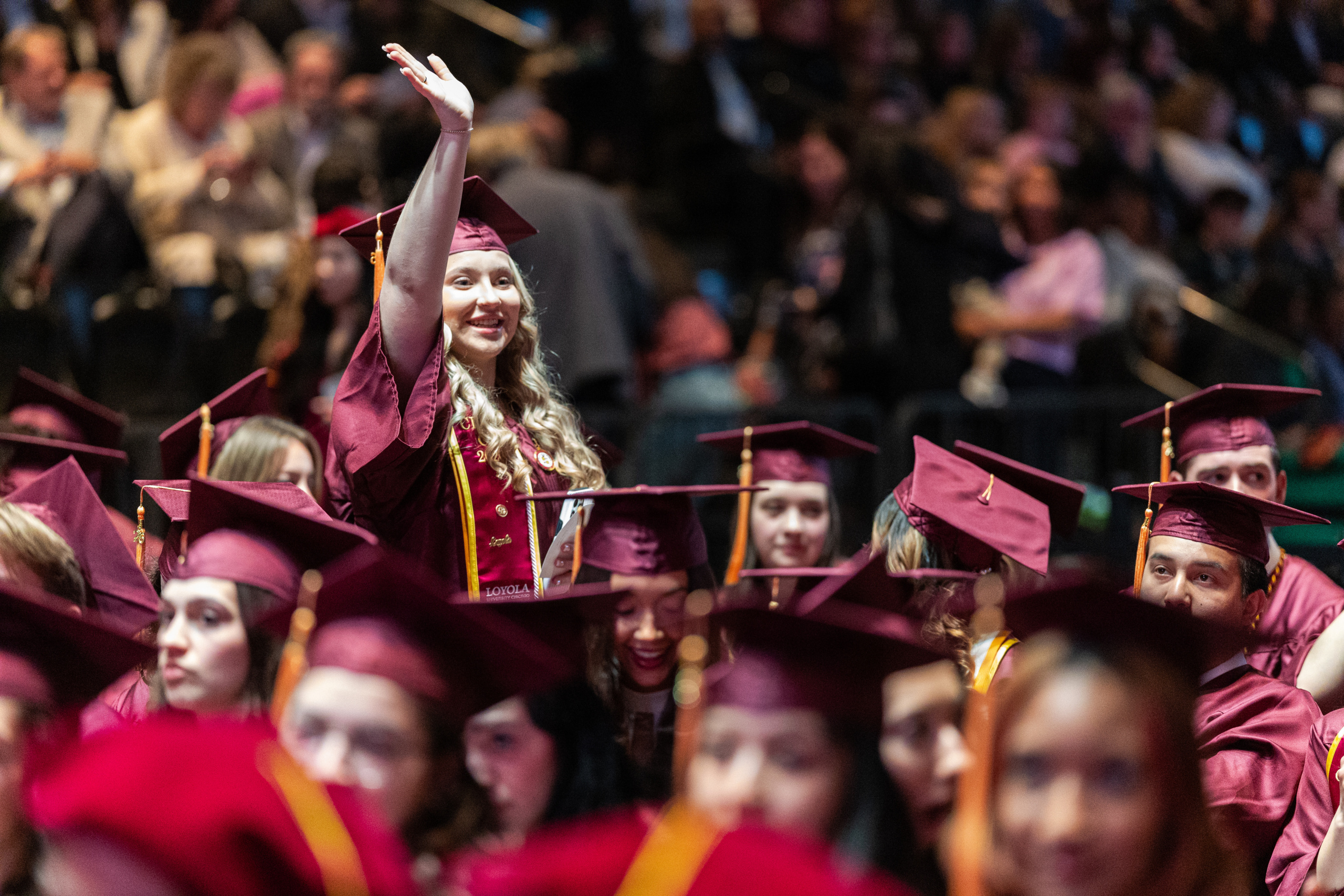 A Loyola University Chicago graduate stands and waves to her family before the Commencement ceremony for the Marcella Niehoff School of Nursing in Gentile Arena on May 6, 2026. Laura Ferrio (MBA '93, MSN '93) RN, CRRN, NEA-BC was the keynote speaker.
