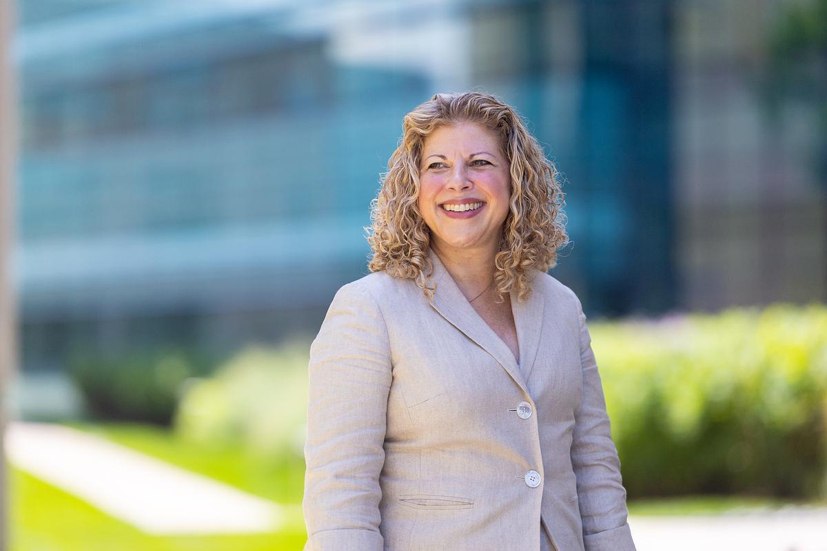 A Loyola University Chicago professor stands in front of campus buildings with green grass and plants in the background.