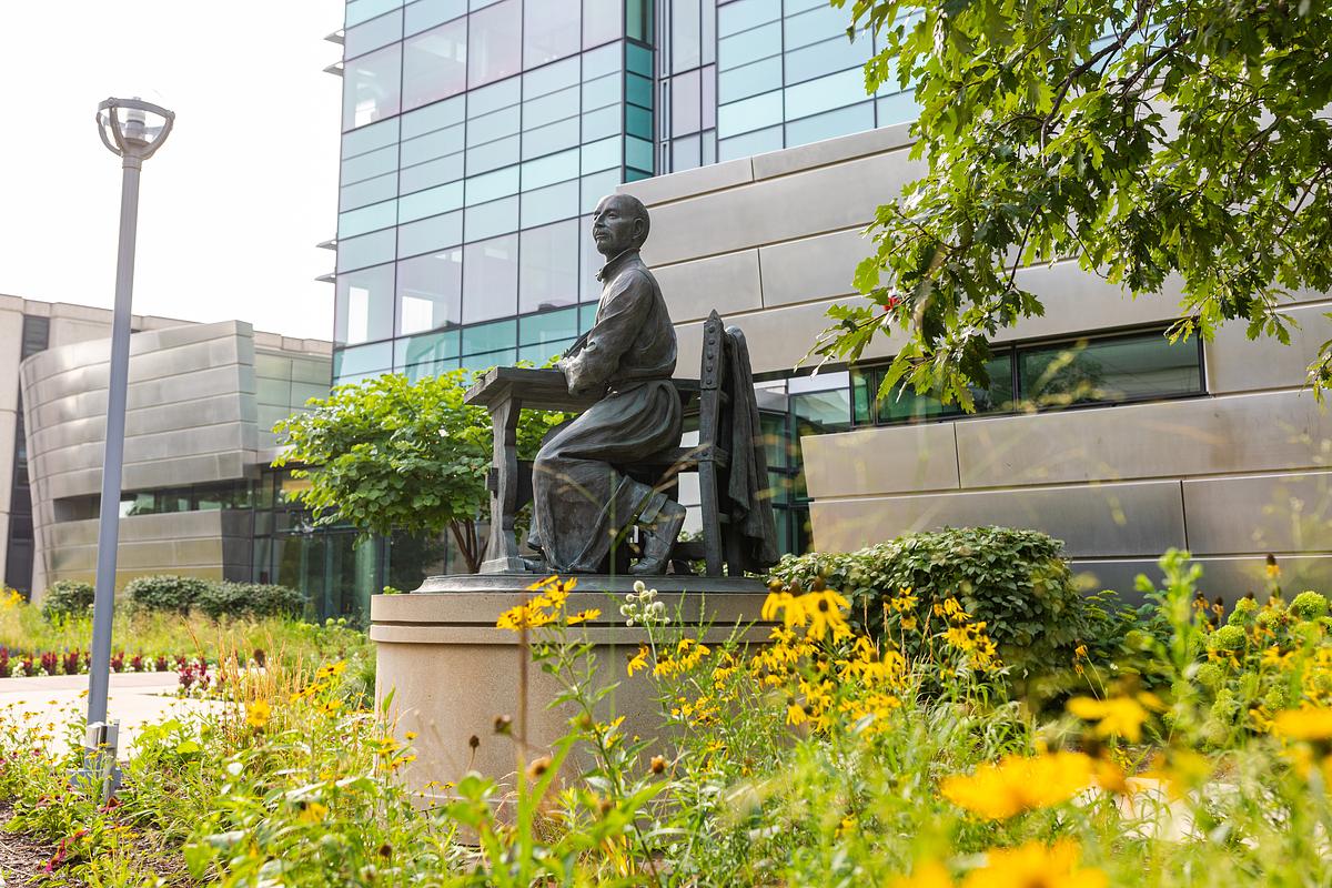 A bronze statue of St. Ignatius of Loyola sits on the Health Sciences Campus of Loyola University Chicago surrounded by late summer flowers.