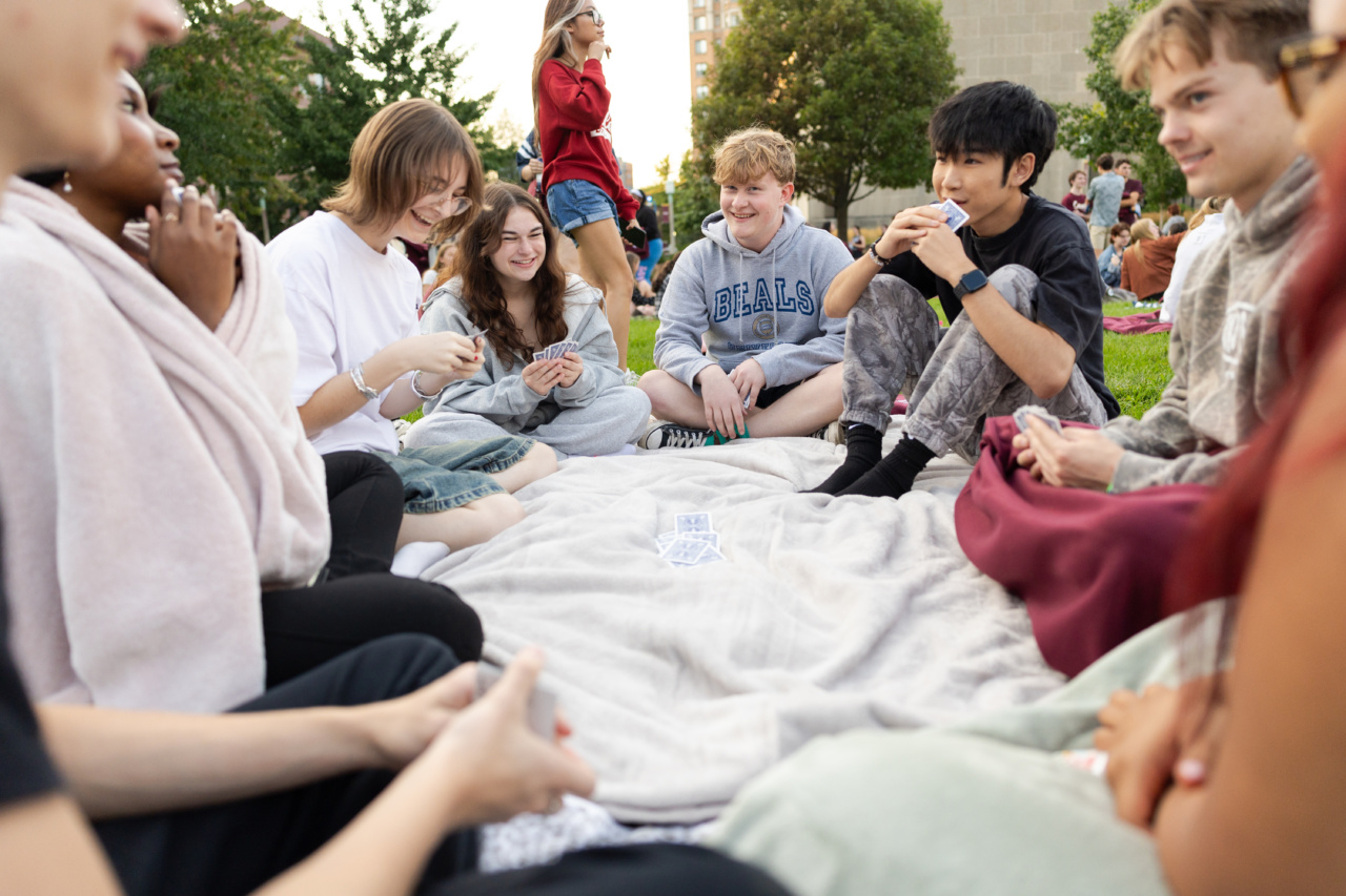 A group of Loyola University Chicago students sits in a circle on a blanket outdoors with a pile of playing cards in the middle