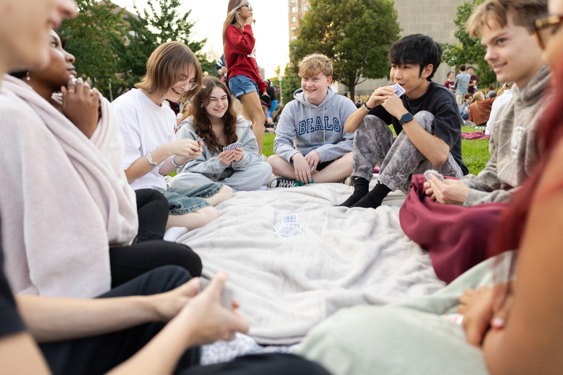 A group of Loyola University Chicago students sits in a circle on a blanket outdoors with a pile of playing cards in the middle